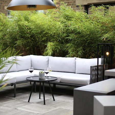 Middle Eight - Covent Garden - Preferred Hotels And Resorts Londra Esterno foto The photo shows an outdoor seating area featuring a modern gray sectional sofa with plush cushions. In front of the sofa is a small, round black table with two glasses of wine on it, accompanied by a decorative plant or vase. Surrounding the area are