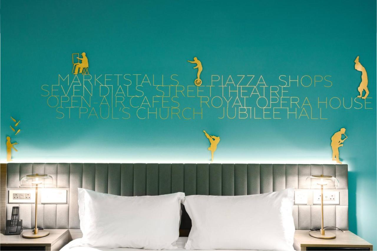 Middle Eight - Covent Garden - Preferred Hotels And Resorts Londra Esterno foto The photo shows a modern hotel room with a distinctive turquoise wall. On the wall, there are gold silhouettes of people engaged in various activities, suggesting movement or leisure. The wall also features text that highlights local attractions like