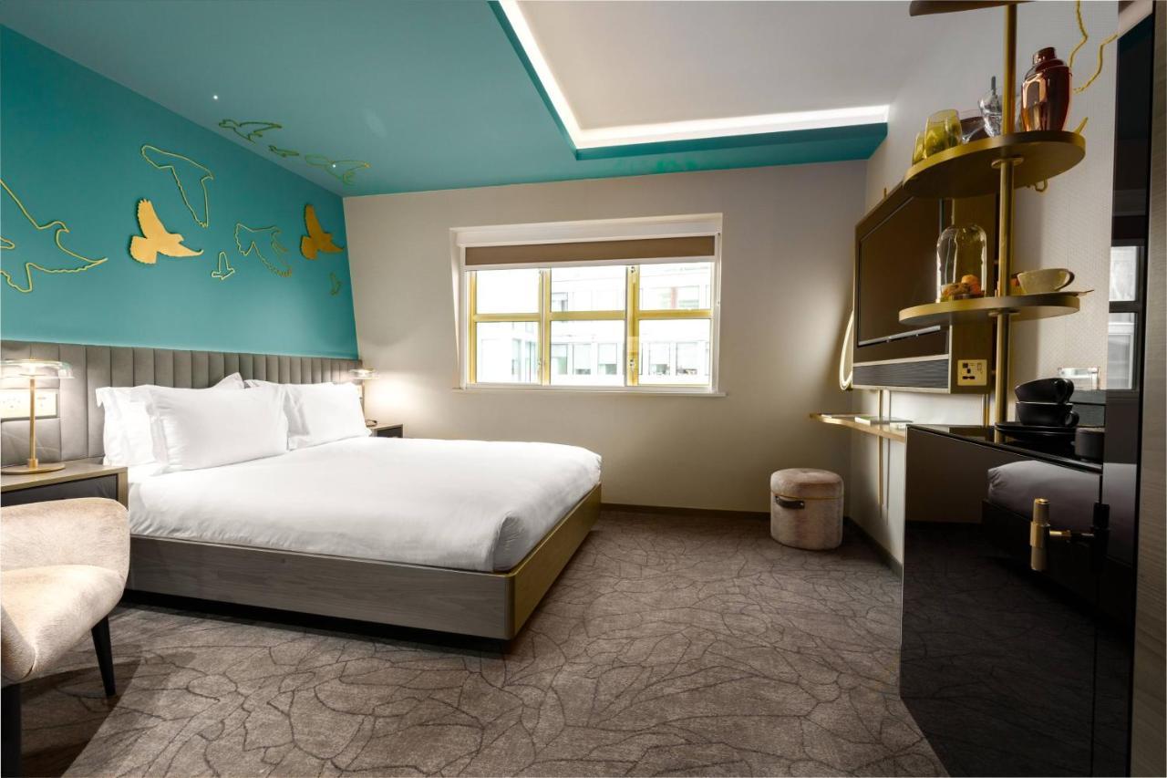 Middle Eight - Covent Garden - Preferred Hotels And Resorts Londra Esterno foto The photo shows a modern hotel room featuring a large bed with white linens positioned against a wall. The decor includes a striking turquoise ceiling and decorative elements, such as yellow motifs, on the wall. There are large windows allowing natur