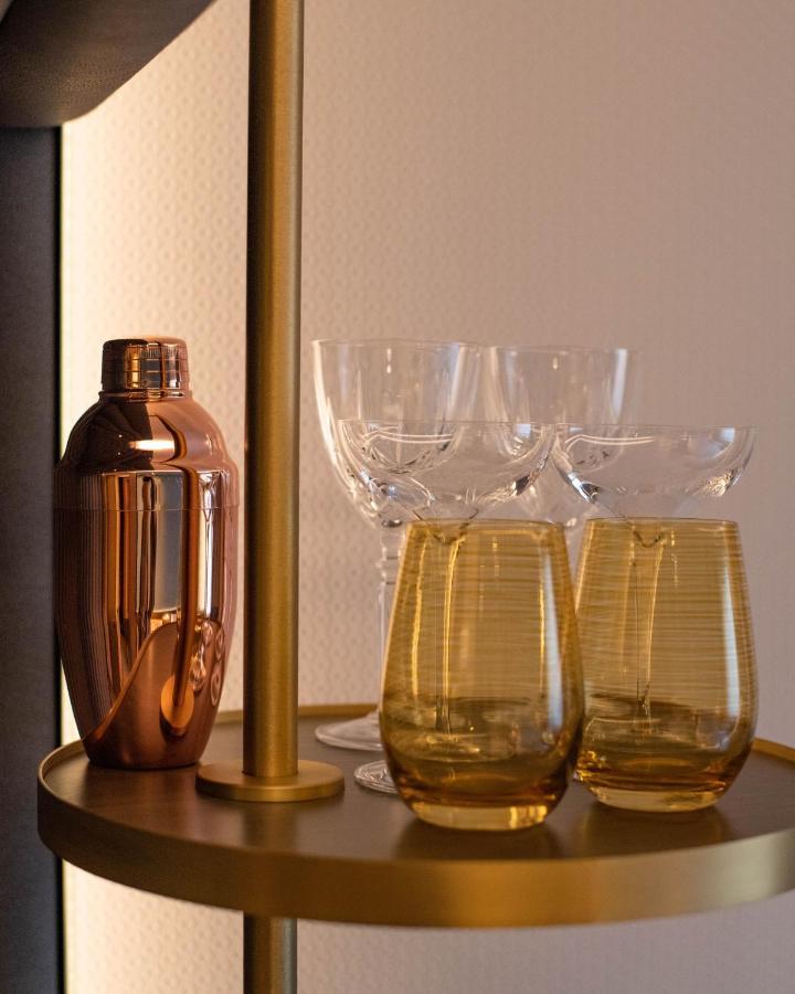 Middle Eight - Covent Garden - Preferred Hotels And Resorts Londra Esterno foto The photo shows a stylish bar setup featuring a shiny copper cocktail shaker positioned next to several elegant glassware pieces. There are four tall, clear stemmed glasses and two round, amber-colored glasses with a textured pattern. The background 