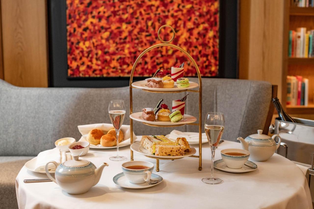 Middle Eight - Covent Garden - Preferred Hotels And Resorts Londra Esterno foto The photo shows an elegant afternoon tea setup on a white tablecloth. At the center, there is a multi-tiered stand displaying a variety of pastries and desserts, including cakes and colorful sweets. Surrounding the stand are teapots and teacups, read