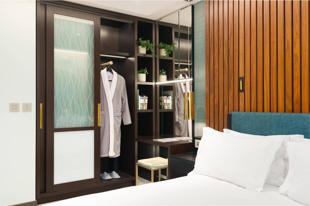 Middle Eight - Covent Garden - Preferred Hotels And Resorts Londra Esterno foto The photo shows a cozy hotel room featuring a neatly made bed with white bedding. On the side, there is a wardrobe with sliding glass doors. Inside the wardrobe, a light-colored robe is hanging, and there are shelves with small plants and toiletries 