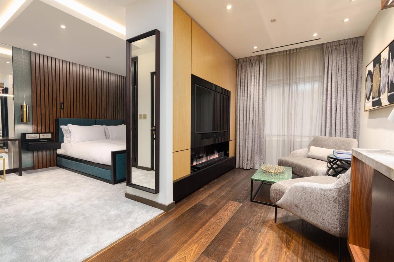 Middle Eight - Covent Garden - Preferred Hotels And Resorts Londra Esterno foto The photo depicts a modern hotel room or suite featuring a cozy living space. On one side, there's a comfortable bed with plush bedding, positioned against a backdrop of elegant wooden paneling. Adjacent to the bed is a contemporary fireplace integra