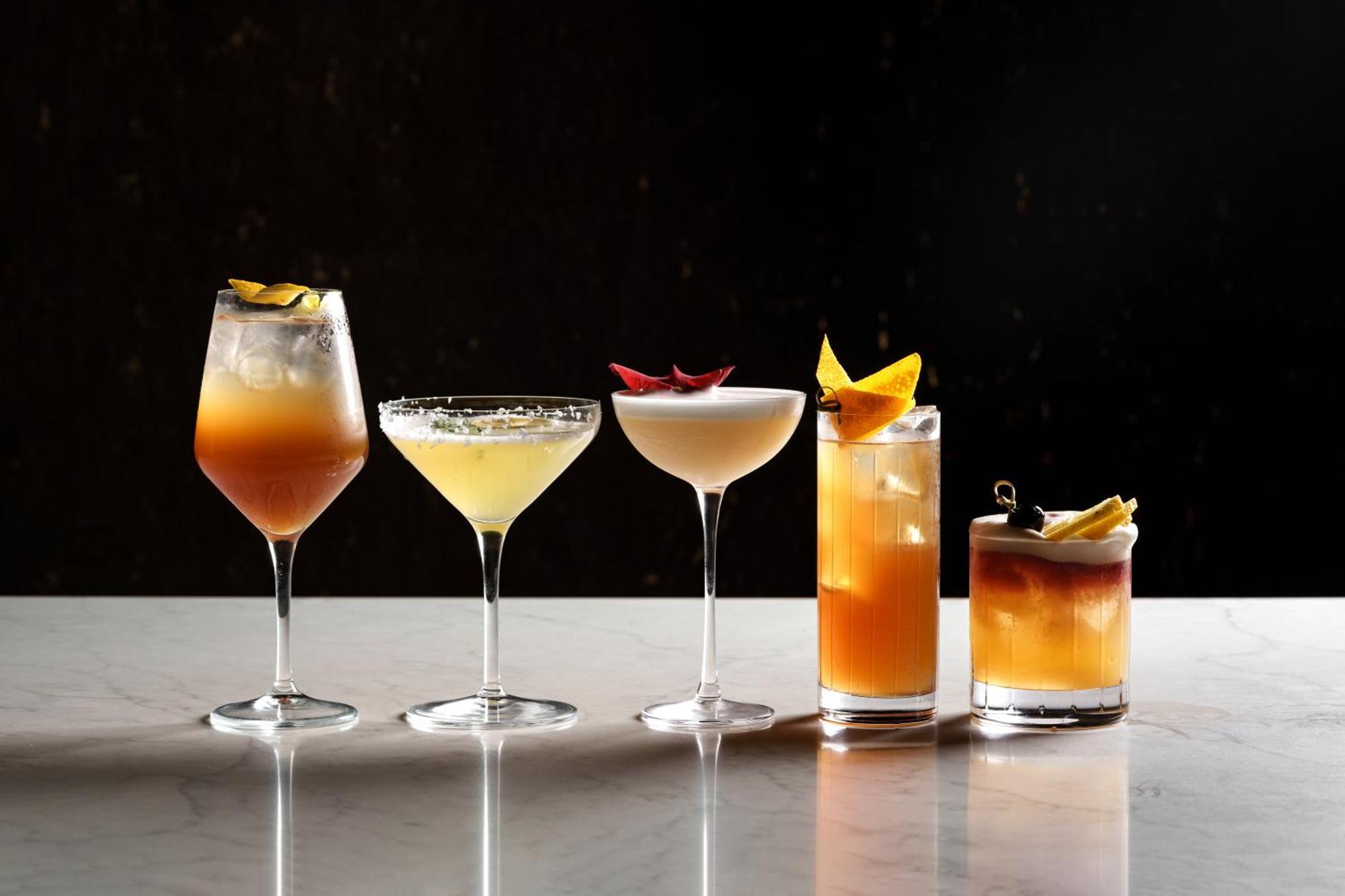 Middle Eight - Covent Garden - Preferred Hotels And Resorts Londra Esterno foto The photo features a selection of five different cocktails lined up on a marble surface. Each drink is served in a distinct glass, showcasing a variety of colors and garnishes. 

1. The first cocktail is in a large wine glass, with a gradient color f