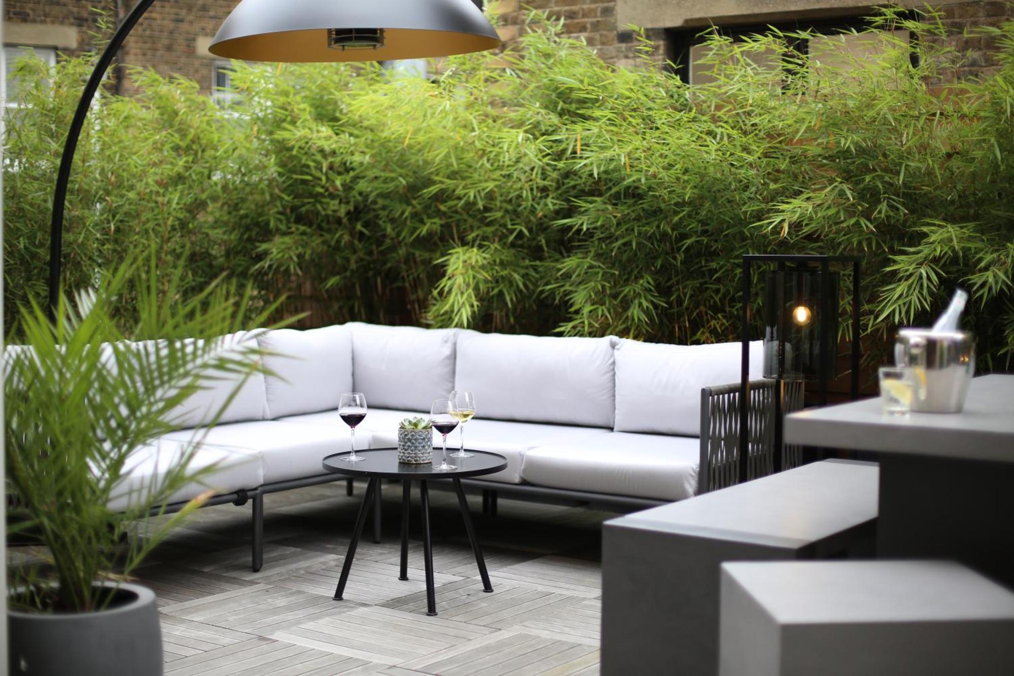 Middle Eight - Covent Garden - Preferred Hotels And Resorts Londra Esterno foto The photo shows an outdoor seating area featuring a modern gray sectional sofa with plush cushions. In front of the sofa is a small, round black table with two glasses of wine on it, accompanied by a decorative plant or vase. Surrounding the area are